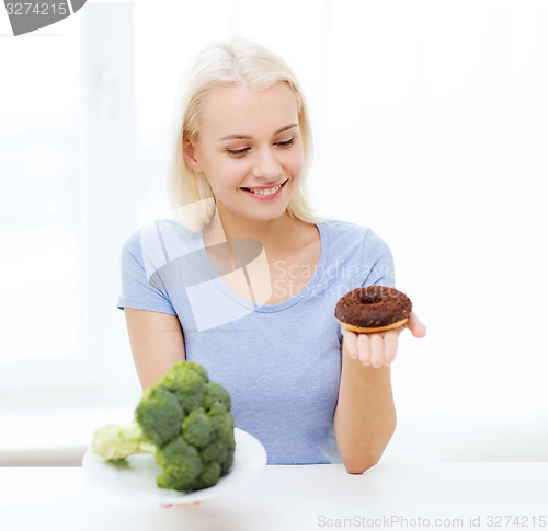 Image of smiling woman with broccoli and donut at home