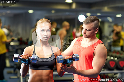 Image of young couple with dumbbells flexing muscles in gym