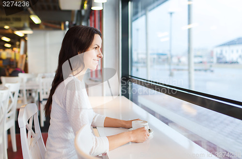 Image of smiling young woman drinking coffee at cafe