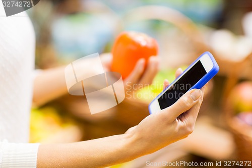 Image of woman with smartphone and persimmon in market