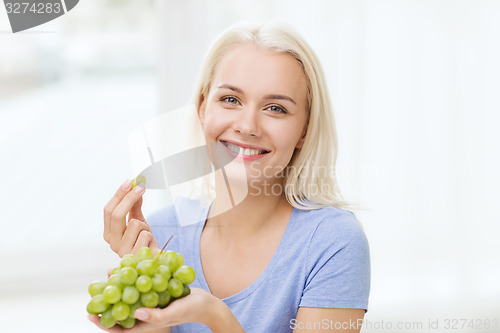 Image of happy woman eating grapes at home