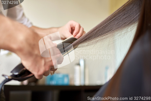 Image of stylist with iron straightening hair at salon