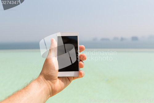 Image of close up of male hand holding smartphone on beach