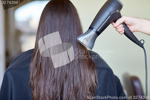 Image of stylist hand with fan dries woman hair at salon