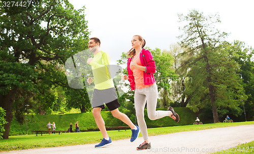 Image of smiling couple with earphones running outdoors