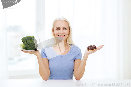 Image of smiling woman with broccoli and donut at home