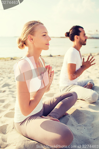 Image of smiling couple making yoga exercises outdoors