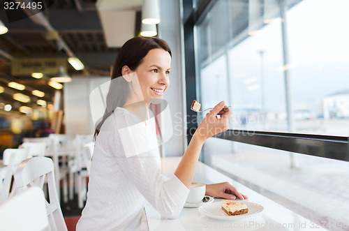 Image of smiling young woman with cake and coffee at cafe