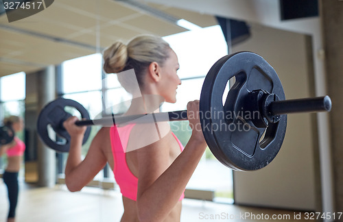 Image of happy woman flexing muscles with barbell in gym