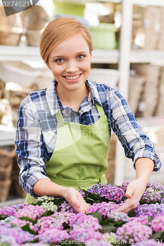 Image of happy woman taking care of flowers in greenhouse