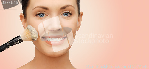 Image of happy woman applying powder foundation with brush
