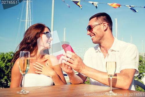 Image of smiling couple with champagne and gift at cafe