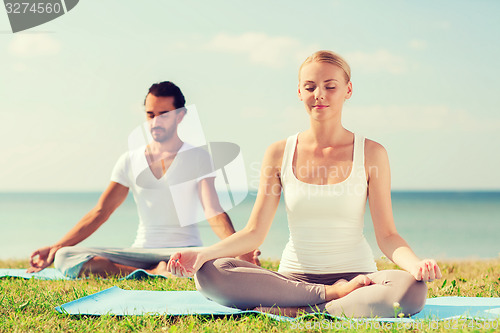 Image of smiling couple making yoga exercises outdoors