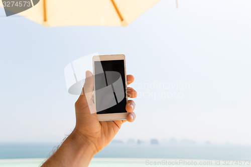 Image of close up of male hand holding smartphone on beach