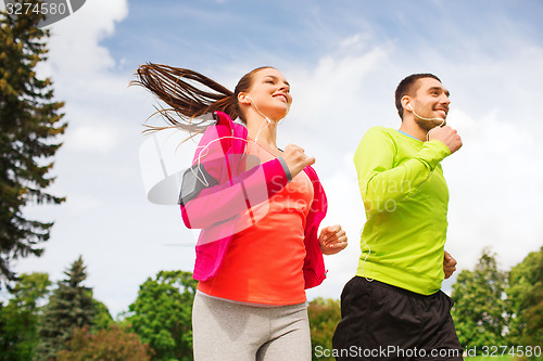 Image of smiling couple with earphones running outdoors