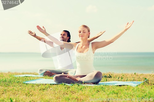 Image of smiling couple making yoga exercises outdoors