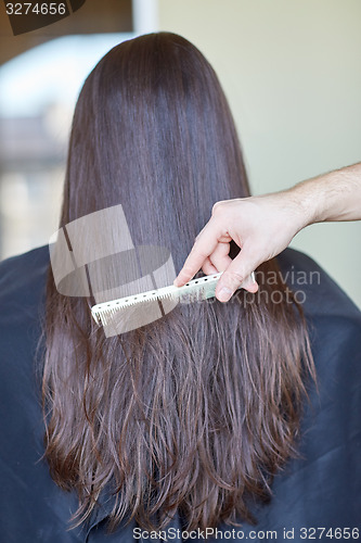 Image of hand with comb combing woman hair at salon