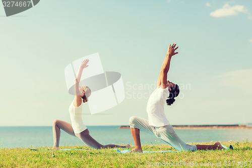 Image of smiling couple making yoga exercises outdoors