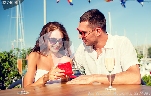 Image of smiling couple with champagne and gift at cafe