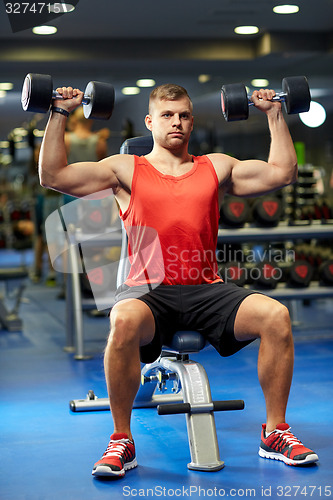 Image of young man with dumbbells flexing muscles in gym