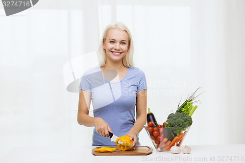 Image of smiling young woman chopping vegetables at home