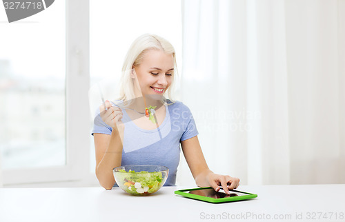 Image of smiling woman eating salad with tablet pc at home