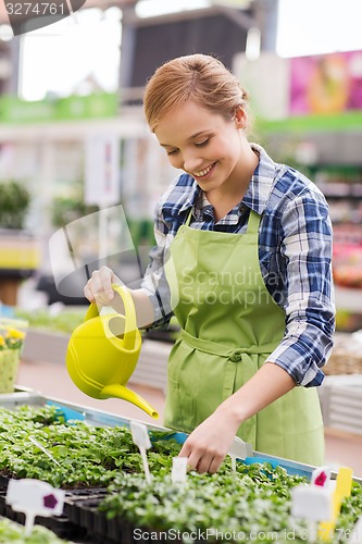 Image of happy woman with watering can in greenhouse