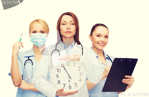 Image of calm female doctor and nurses with wall clock