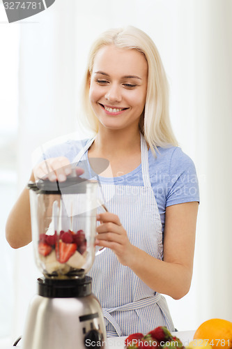 Image of smiling woman with blender preparing shake at home