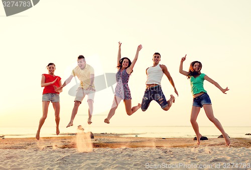Image of smiling friends dancing and jumping on beach