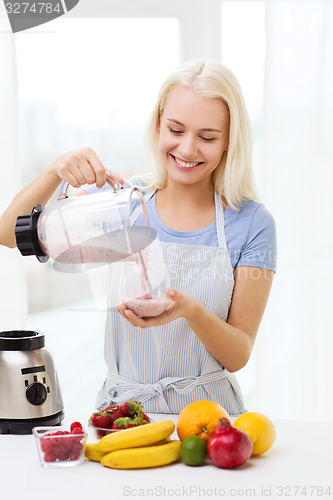 Image of smiling woman with blender preparing shake at home