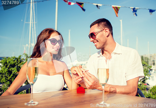 Image of smiling couple with champagne and gift at cafe