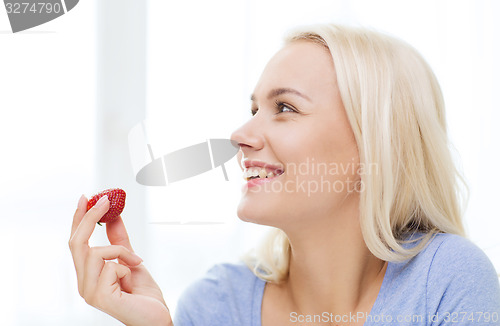 Image of happy woman eating strawberry at home