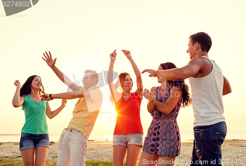 Image of smiling friends dancing on summer beach