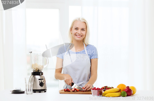 Image of smiling woman with blender preparing shake at home