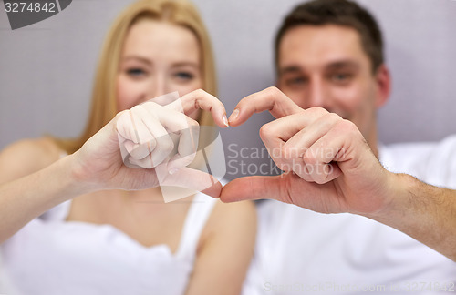 Image of smiling couple in bed making heart shape gesture