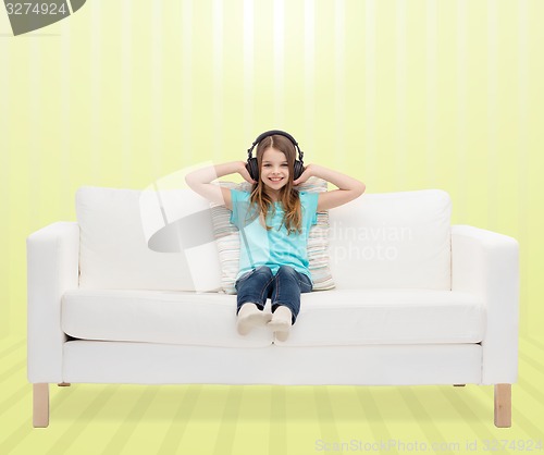 Image of smiling little girl in headphones sitting on sofa