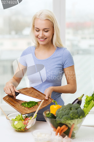 Image of smiling woman cooking vegetable salad at home