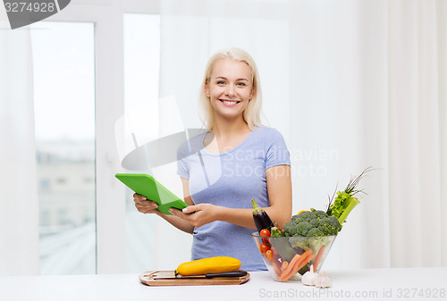 Image of smiling young woman with tablet pc cooking at home