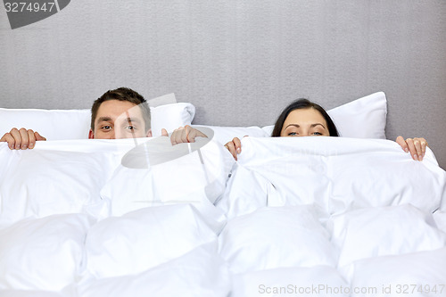 Image of happy couple hiding under blanket in bed