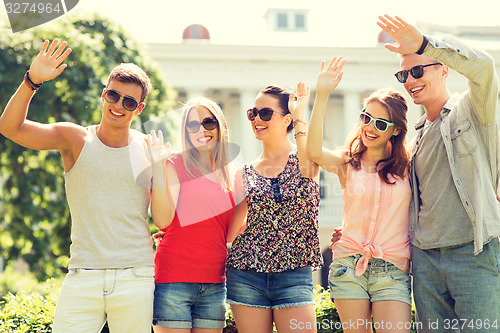 Image of group of smiling friends waving hands outdoors