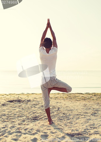 Image of man making yoga exercises outdoors from back