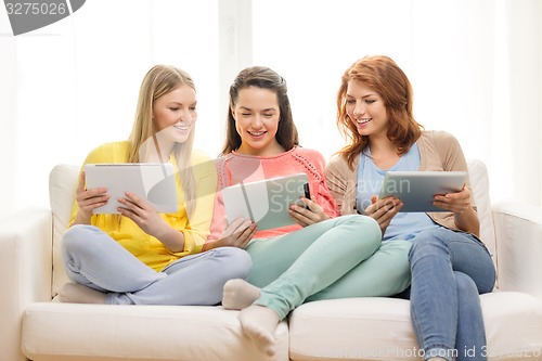 Image of three smiling teenage girls with tablet pc at home
