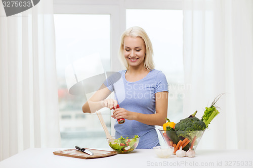 Image of smiling woman cooking vegetable salad at home