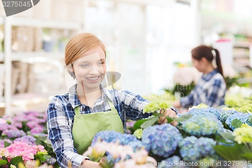 Image of happy woman taking care of flowers in greenhouse