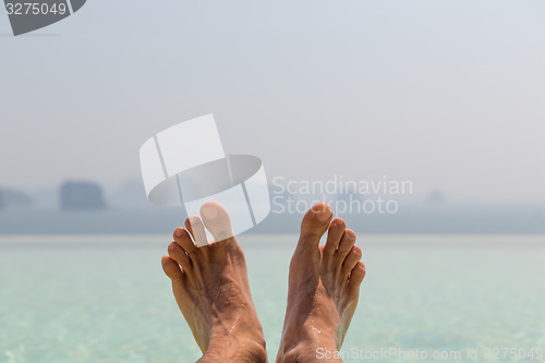 Image of closeup of male feet over sea and sky on beach