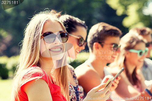 Image of smiling friends with smartphones sitting in park