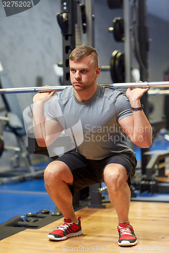 Image of young man flexing muscles with barbell in gym