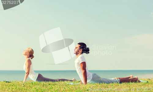 Image of smiling couple making yoga exercises outdoors