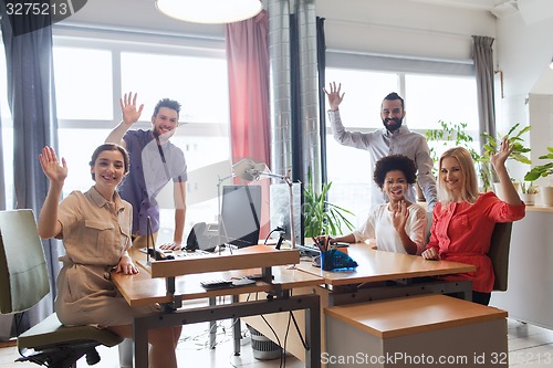 Image of happy creative team waving hands in office